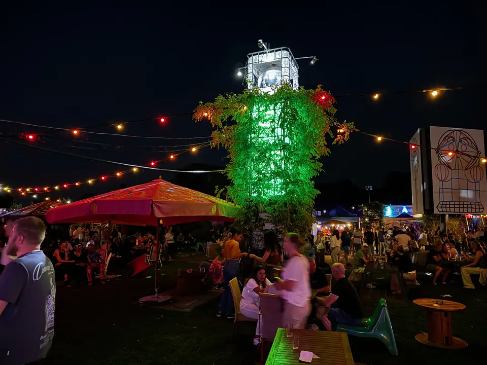 Een avondsfeer op Oogst met lichtsnoeren, een groene toren en bezoekers op het terrein