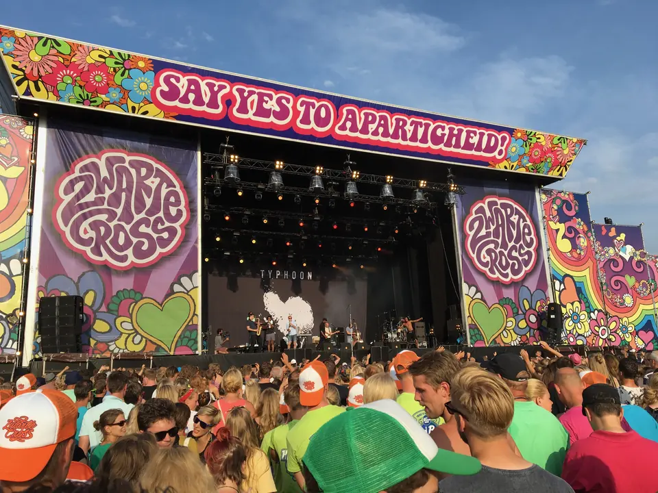 Het kleurrijke hoofdpodium van Zwarte Cross met de tekst Say yes to apartheid en publiek ervoor